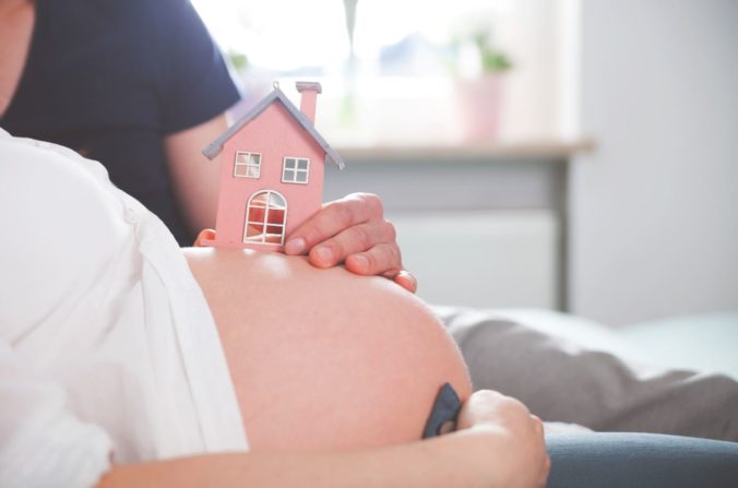 Frau mit gebasteltem Haus auf Schwangerschaftsbauch