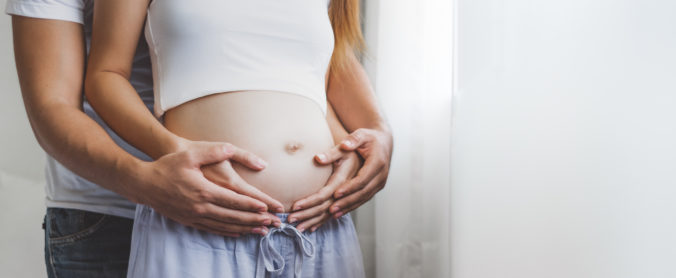 Mann umschließt mit den Händen Bauch seiner schwangeren Frau