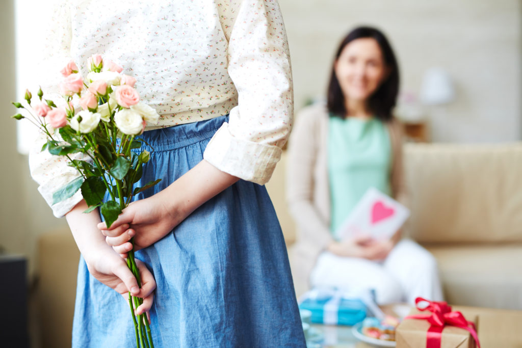 Mädchen hält Blumen für ihre Mutter hinter dem Rücken