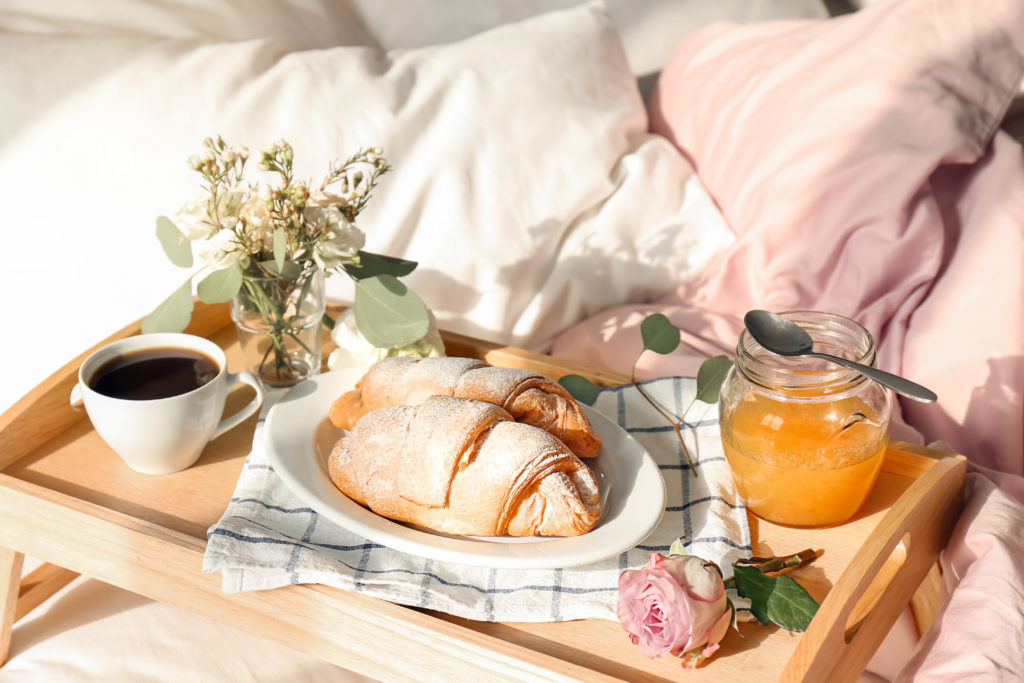 Frühstückstablett mit Croissants, Kaffee, Saft und Blumen auf dem Bett