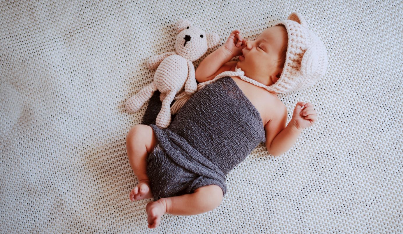 Baby mit Strickteddy und Strickmütze