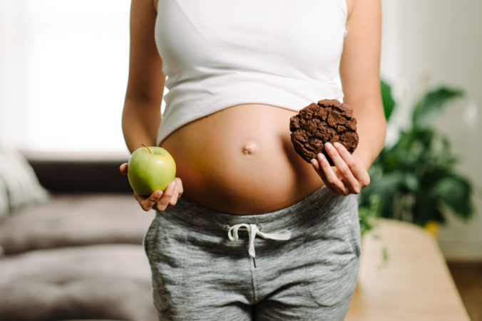 Schwangere mit Keks und Apfel in der Hand