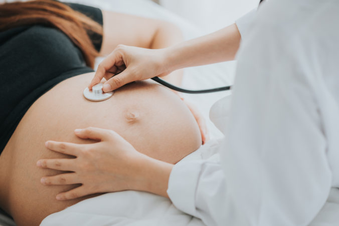 Dokot hält Stethoskop auf Bauch von Schwangeren