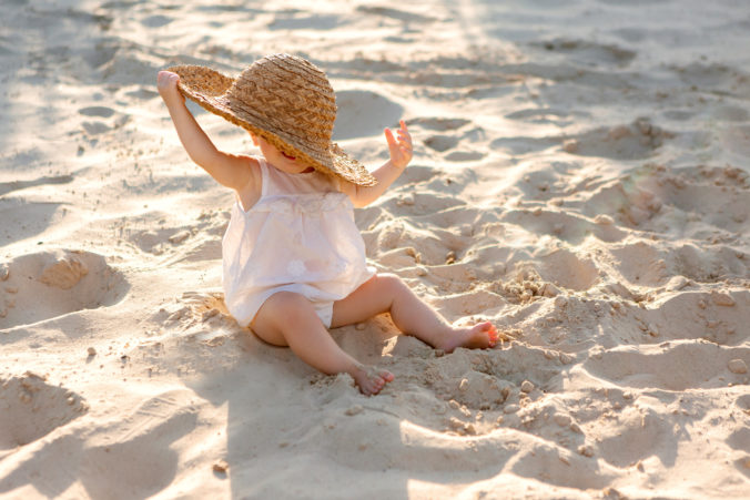 Baby sitzt mit Hut am Strand