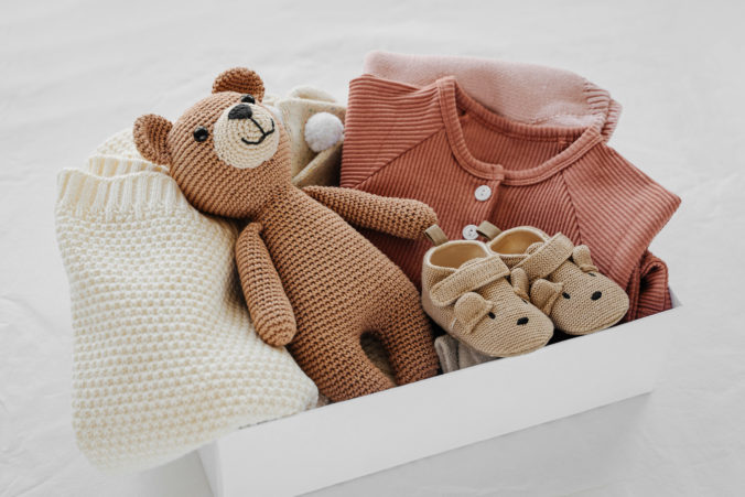 Kiste mit Teddybär, Babyschuhen und Babykleidung