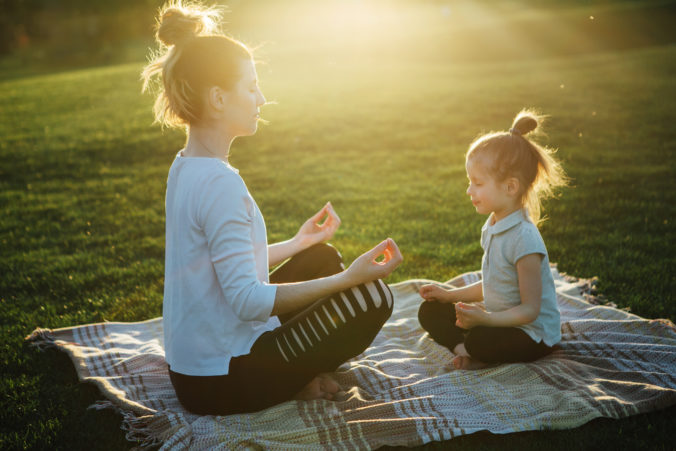 Mama und kleine Tochter meditieren im Park bei Sonnenaufgang