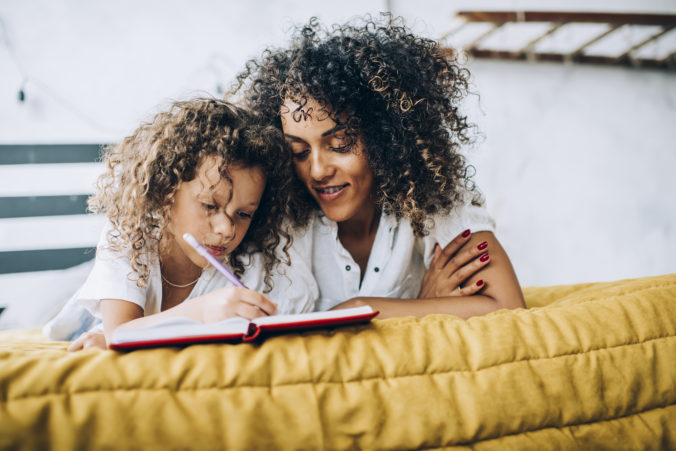 Mama und Kind liegen zusammen im BEtt und schreiben etwas in ein Buch