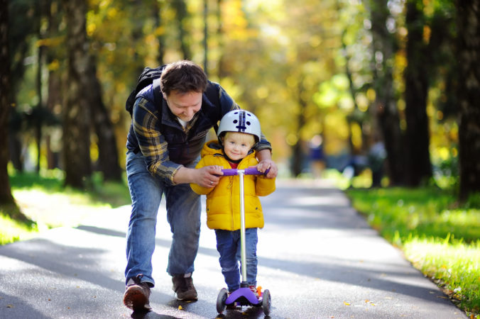 Vater übt mit Kind rollerfahren im Park