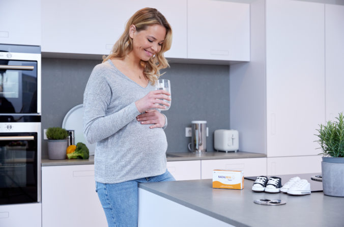 Schwangere Frau trinkt Wasser in der Küche