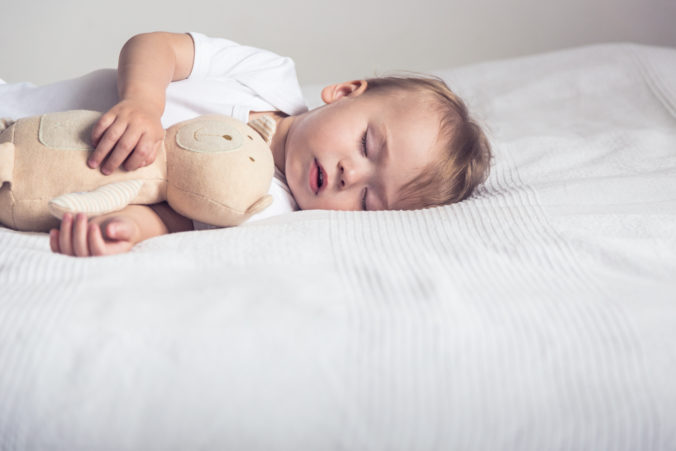 Schlafendes Baby mit Kuscheltier im Kinderbett