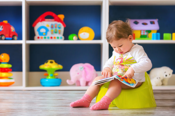 Kleines Mädchen sitzt in ihrem Zimmer und schaut sich ein Buch an