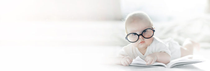 Auf dem Bauch liegendes Baby mit Brille liest ein Buch