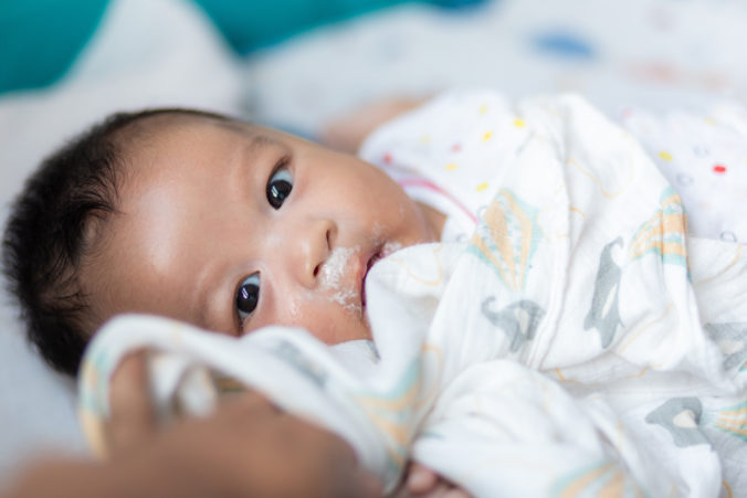 Krankes Baby liegt auf dem Bett nachdem es Milch ausgespuckt hat 