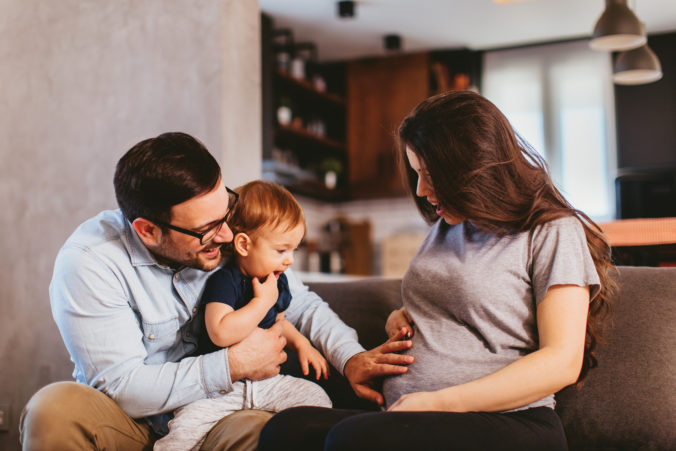 Kleine glückliche Familie freut sich auf Zuwachs und berührt den Babybauch der Mutter