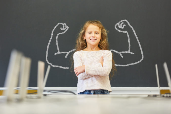 Lächelndes Mädchen in der Schule steht vor einer Tafel mit Muskeln aus Kreide