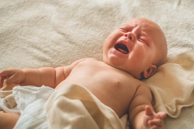 Weinendes Baby liegt auf dem Bett 