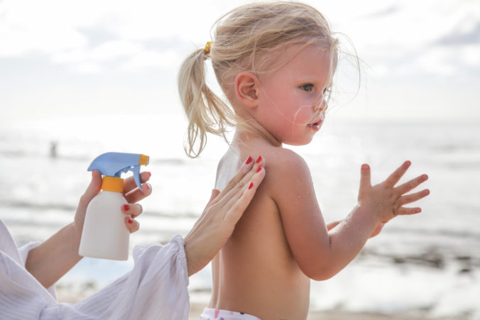 Mutter cremt ihrer Tochter den Rücken mit Sonnencreme ein 