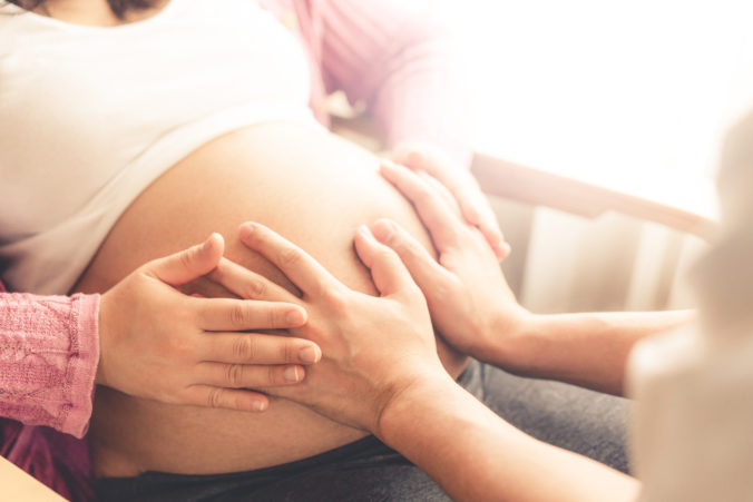 Hände liegen auf Bauch einer schwangeren Frau